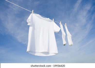 A white blank t-shirt hanging on a clothesline in front of a blue sky background with copy space - Powered by Shutterstock