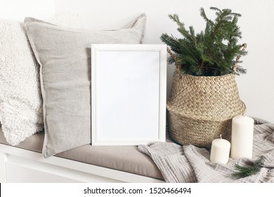 White blank wooden frame mockup with Christmas tree, candles, linen cushions and plaid on the white bench. Poster product design. Scandinavian home decor, nordic design. Winter festive concept.
