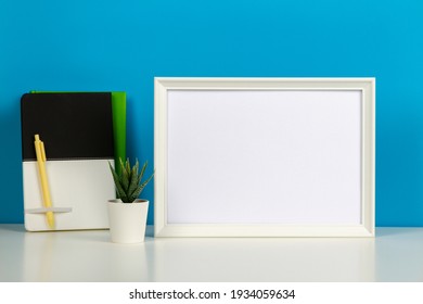 White Blank Wooden Mock Up Frame On Twhite Desk With Paper Notebook Book, Blue Background