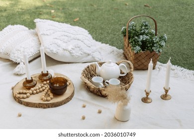 White Blanket At Green Grass, Outdoor Decor For Picnic. Pillows, Dishes, Wooden Decoration At Summer Park. Closeup At Decorative Rustic Things With Nobody Outside.