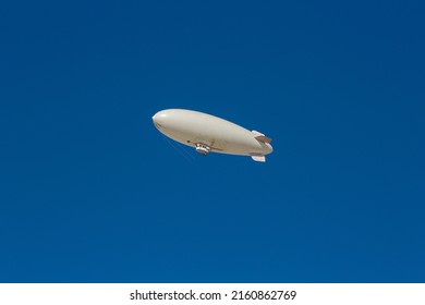 A white blimp, airship, or dirigible flying in blue sky. Close up detail of an unmarked zeppelin like flying vehicle. Flying high above in clear skies.  