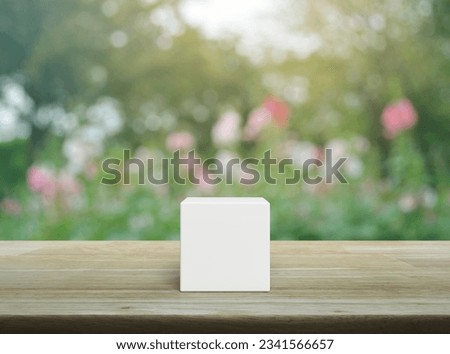 White block cube on wooden table over blur pink flower and tree in garden