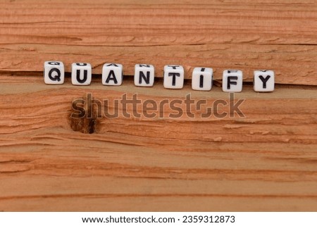 White blocks with black lettering spelling the word Quantify.  Rough natural wooden background. 