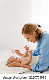 White Blonde Woman Brushing And Swaddling Her Baby In Bedroom At Home