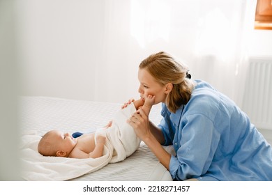 White Blonde Woman Playing And Swaddling Her Baby In Bedroom At Home