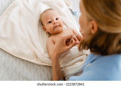 White Blonde Woman Playing And Swaddling Her Baby In Bedroom At Home