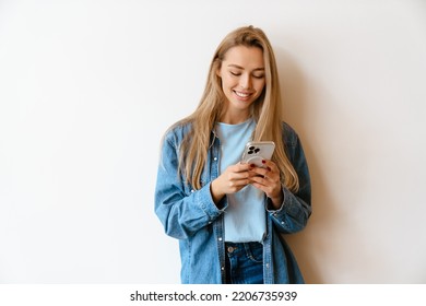 White blonde woman using mobile phone while standing by wall indoors - Powered by Shutterstock