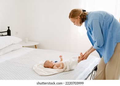 White Blonde Woman Wearing Shirt Swaddling Her Baby In Bedroom At Home