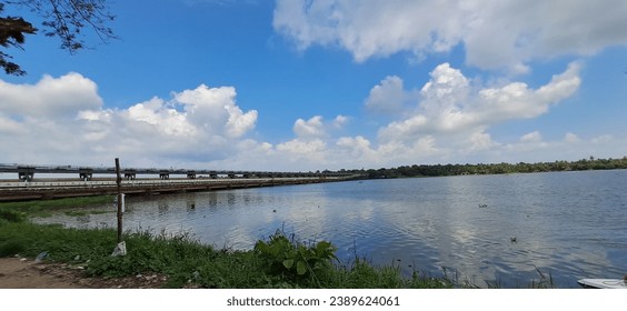 A white and blue boat is gently floating down a tranquil river, with a concrete bridge in the background - Powered by Shutterstock