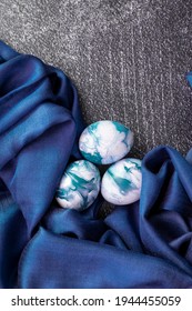 White And Blue Handprinted Easter Eggs Folded In Blue Silky Scarf On Dark Background