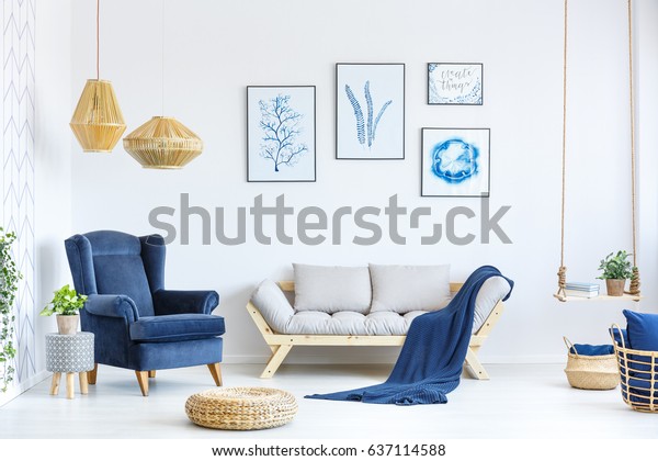 White and blue living room with sofa, armchair,\
lamp, posters