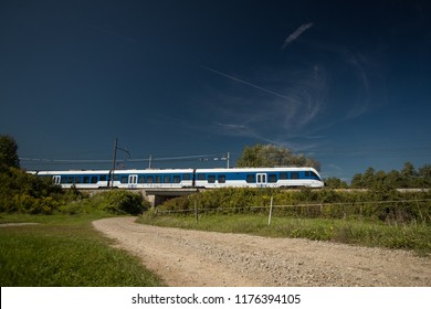 White and blue passenger train running between Udine, Trieste and Ljubljana close to Preserje train station driving over a small bridge on a sunny day. - Shutterstock ID 1176394105