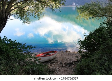 white boat on the shore of Lake Scanno, Abruzzo. Colorful reflections on the water in a summer landscape surrounded by nature. Frame of green vegetation. Glimpse of calm, tranquility and relaxation. - Shutterstock ID 1784756387
