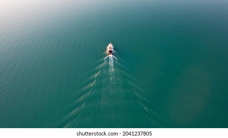 A white boat sails on Lake Balkhash at sunset. A beautiful long train on the water from the motor. The sky gradient is from orange to blue. Smooth water. Travel on a speed bot. Bertys Bay. Kazakhstan - Powered by Shutterstock