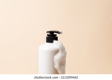 White Body Wash Dispenser With Black Pump Type And Some Of Bubbles On Peach Colored Background