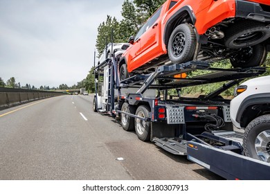 White bonnet industrial grade big rig car hauler semi truck tractor transporting cars on specialized two level modular hydraulic semi trailer driving on the wide highway road with trees on the side