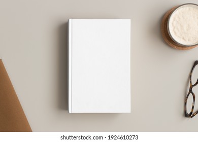 White book mockup with a coffee and workspace accessories on a beige table.