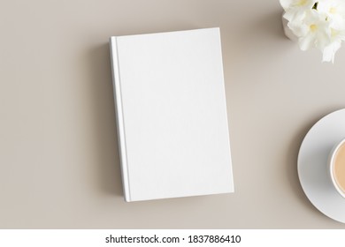 White Book Mockup With A Cup Of Coffee And Oleander On A Beige Table.