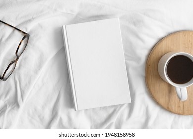 White Book Mockup With A Cup Of Coffee And A Glasses On The Bed.
