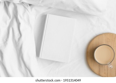 White book mockup with a cup of coffee on the bed.
