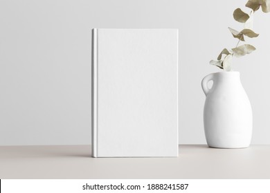 White Book Mockup With A Eucalyptus In A Vase On A Beige Table.