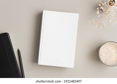 White book mockup with a gypsophila, coffee and workspace accessories on a beige table.