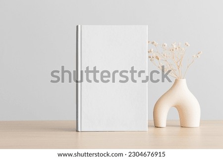 White book mockup with a gypsophila decoration on the wooden table.