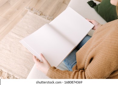 Das weiße Buch ist verspottet. Geöffnetes quadratisches leeres Buch. Album mit sauberen Seiten in den Händen der Frau. Saubere Buchbesatz. Frau sitzt auf dem Sofa mit einem Buch. Mock up ist bereit für Design