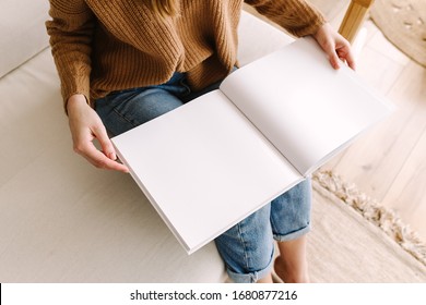 Das weiße Buch ist verspottet. Geöffnetes quadratisches leeres Buch. Album mit sauberen Seiten in den Händen der Frau. Saubere Buchbesatz. Frau sitzt auf dem Sofa mit einem Buch. Mock up ist bereit für Design