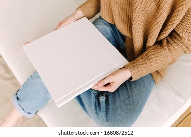 Das weiße Buch ist verspottet. Platz leeres Buch. Album mit sauberen Seiten in den Händen der Frau. Saubere Buchcover-Muster. Frau sitzt auf dem Sofa mit einem Buch. Mock up ist bereit für Design