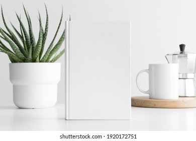 White book mockup with a succulent plant and a mug on a white table.