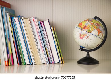 White Book Rack With Many Colorful Books And Small Globe On Black Stand. Back To School, Alarm Clock And Sketch Pen Set, Horizontal View, With Books For Kids In Room For Children