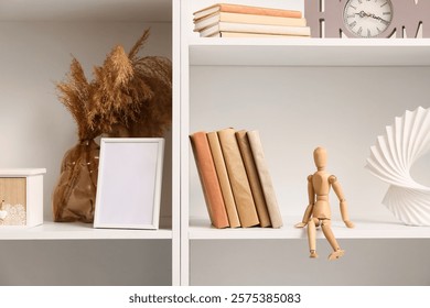 White bookshelf with decorative elements including a wooden mannequin, books, and dried pampas grass in a vase