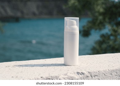 A white bottle with a cream dispenser stands on a white surface, with the sea and mountains in the background. Clean template for brand presentation.