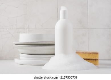 White Bottle With Dishwashing Detergent And Soap Suds. Plates In The Background. Washing Dishes In The Kitchen, Cleaning Concept