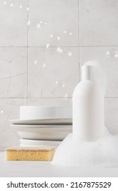 White Bottle With Dishwashing Detergent And Soap Suds. Plates In The Background. Washing Dishes In The Kitchen, Cleaning Concept