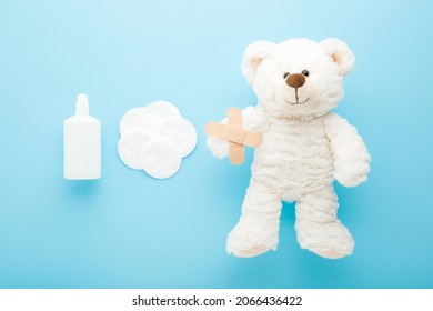 White Bottle Of Hydrogen Peroxide, Cleansing Cotton Pads And Adhesive Bandages And Fluffy Teddy Bear Light Blue Table Background. Pastel Color. Medical Kit For Skin Wound Cleaning Of Children.