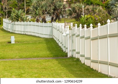 White Boundary Vertical Slat Plastic Pvc Fence Along Roadside Grass Landscape.