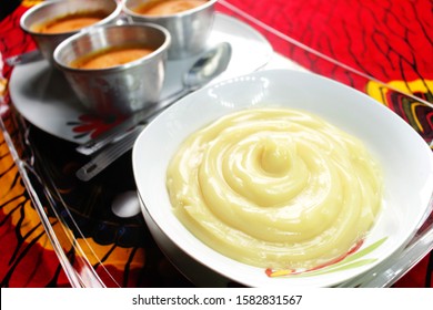 A White Bowl Of African Cereal Or Nigerian Food, Pap (Ogi) Placed In A Tray On A Red And Yellow Colorful Pattern Tablecloth