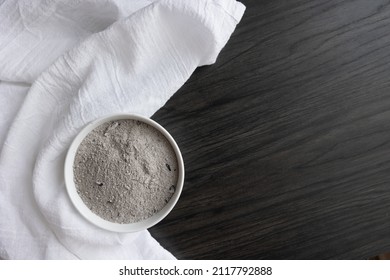 White bowl of ashes and white linen on dark wood with copy space