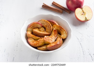 A white bowl of baked apple slices with cinnamon on a light blue background. Delicious homemade vegan dessert - Powered by Shutterstock