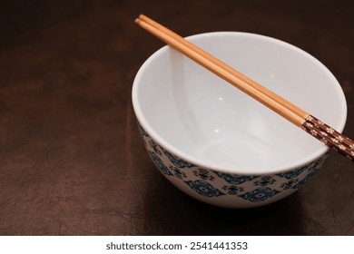 White bowl with blue pattern outside and wooden chopsticks on brown background, traditional wooden sticks for asian food.  - Powered by Shutterstock