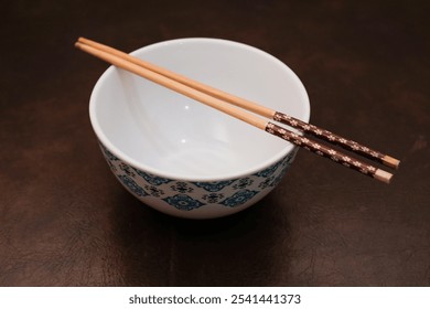 White bowl with blue pattern outside and wooden chopsticks on brown background, traditional wooden sticks for asian food.  - Powered by Shutterstock