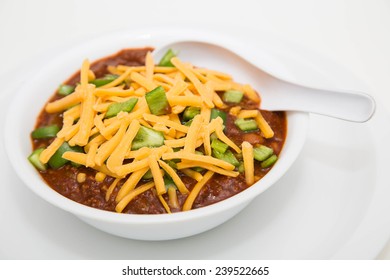 A White Bowl Of Chilli With Meat And Beans And Green Poblano Chile Peppers Topped With Shredded Cheddar Cheese