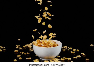 white bowl with cornflakes and fallen pieces isolated on black