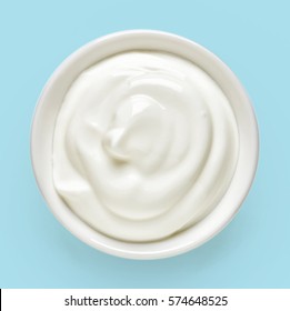 White bowl of cream on light blue background, top view