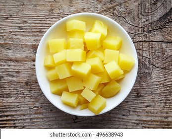 White bowl of diced boiled potatoes on wooden table, top view