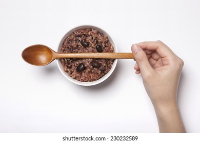 A White Bowl With Multi-grain Rice And Wood Spoon And Hand Isolated White Top View At The Studio.