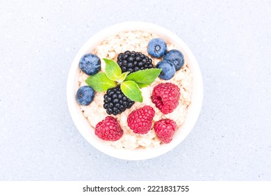 White Bowl With Oatmeal Porridge Served With Raspberries, Blueberries And Blackberries On Concrete Table Background. Morning Superfood Porridge Recipe. Healthy Breakfast. View Above