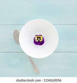 White Bowl With Pansy Flower On Mint Wooden Background. Overhead Food Shots. Clean Eating Concept.